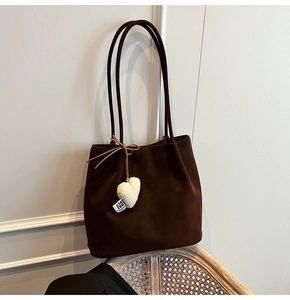 Detail of dark brown faux suede tote bag with plush heart charm on a woven chair