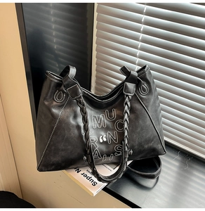 Detail of black tote bag featuring white letters design and woven handles in natural sunlight