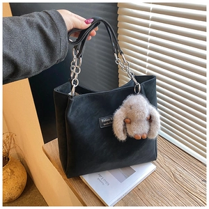 Detail of black tote bag with silver chain handle and plush rabbit charm on side