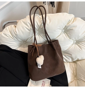 Detail view of coffee suede tote bag featuring a white heart plush charm and long strap