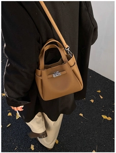 Detailed view of a tan pebble leather bucket bag with metallic twist-lock on street