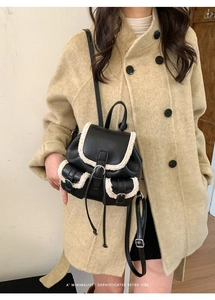 Detail of black leather mini backpack with white fleece trim worn over a beige wool coat