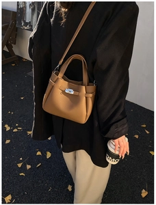 Detail view of caramel brown litchi grain bucket bag with metallic twist lock on black suit