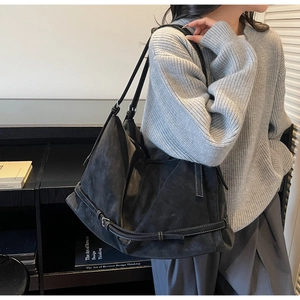 Detail of a black suede tote bag featuring white contrast stitching and buckle strap detail