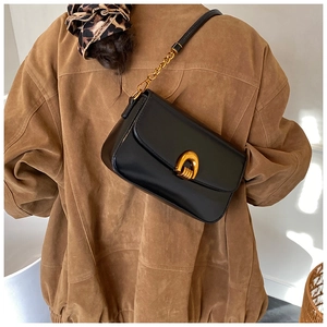 Detail of elegant black leather square bag with golden horseshoe clasp on model