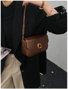 Detailed view of deep brown glossy leather shoulder bag with golden horseshoe buckle