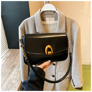 Detail of elegant black glossy leather bag featuring a gold horseshoe-shaped clasp and chain