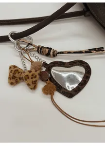 Close-up of leopard print heart mirror charm with bow and pompom on a stylish handbag
