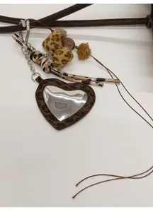 Detail of leopard print heart mirror bag charm with plush pompom and leather strap