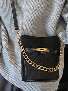 Sac seau matelassé noir chic avec chaîne dorée et bandoulière porté par un mannequin