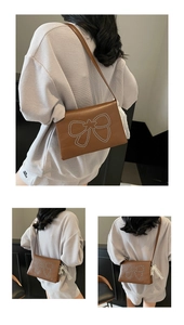 Detail view of brown leather crossbody bag with silver stud bow and white tassel charm