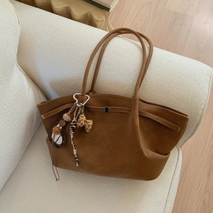 Close-up of brown suede tote bag with leopard bow charm on a cozy beige sofa