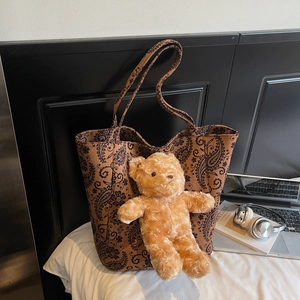 Dettaglio borsa shopper paisley con ciondolo a orsetto su letto bianco