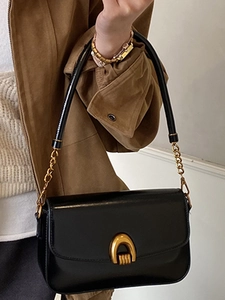 Minimalist black leather shoulder bag with gold arch buckle and chain strap shown on model