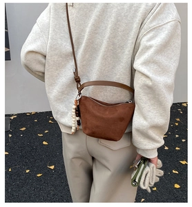 Detalle de bolso cubo de cuero mate marrón con cuentas de madera sobre fondo otoñal suave