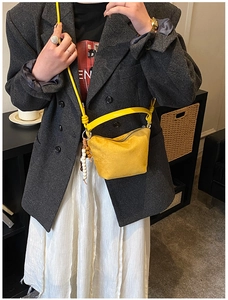 Gelbe Eimer-Tasche aus Mattleder mit Holzperlen-Anhänger und zwei Trageriemen am Modell