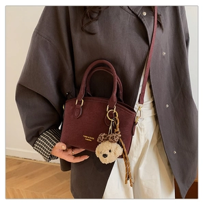 Close-up of burgundy leather crossbody bag featuring a plush bear charm and gold lettering