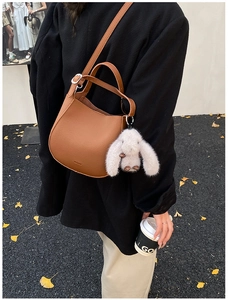 Close-up of brown litchi grain leather bucket bag with a plush white bunny charm