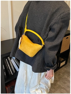 Detalle de bolso tipo cubo de ante amarillo con charm minimalista de cuentas de madera