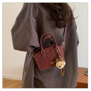Detail of burgundy suede handbag with gold lettering and cute leopard bow bear charm