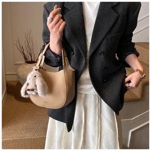 Detail of beige crescent shoulder bag with litchi texture and cute rabbit charm decoration