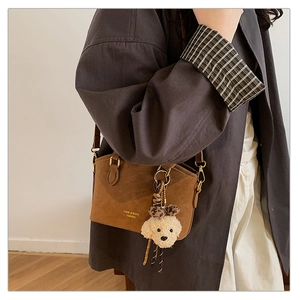 Close-up of brown vintage crossbody bag featuring golden buckle and plush puppy charm