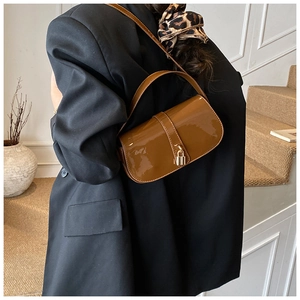 Close-up of caramel patent leather shoulder bag with glossy finish and gold metal buckle