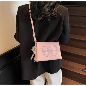 Detail of pink crossbody bag with silver rivet bow and white lace pearl pendant