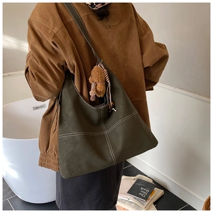 Detail of dark green crossbody tote bag with white contrast stitching and a plush bear charm