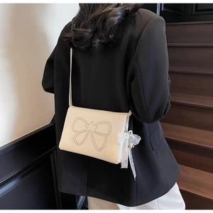 Chic off-white crossbody bag with silver rivet bow and lace pearl charm on a model