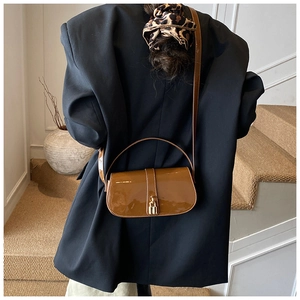 Detail of caramel brown patent leather crossbody bag with gold buckle on black blazer
