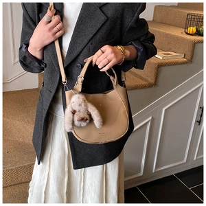 Detail of beige pebble leather shoulder bag with a cute plush rabbit charm on the strap