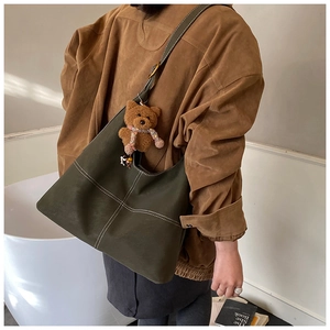 Detail of olive green leather tote featuring white stitching and brown plush bear charm