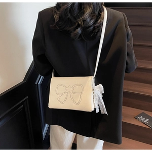 Detail of cream crossbody bag with silver rivet bow and white lace bow pendant