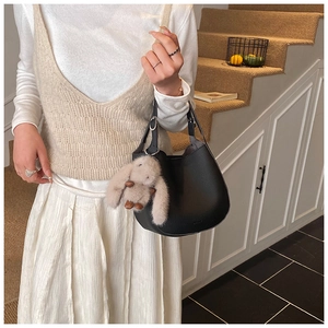 Detail of black pebbled leather bucket bag with a cute plush bunny charm and dual handles