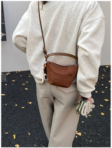 Detalle de un bolso de media luna en ante marrón oscuro con un colgante de cuentas decorativo