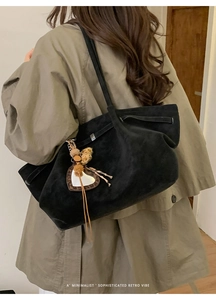 Detail of black suede tote bag with leopard heart charm worn by model in a soft room