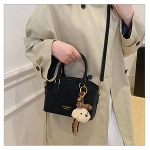 Detail of elegant black crossbody bag with leopard bow bear charm on a female model