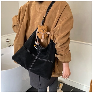 Detail view of black suede tote bag with white stitching and cute teddy bear charm