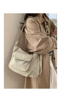 Detail of a beige nylon tote bag featuring a textured surface and functional front flap pocket