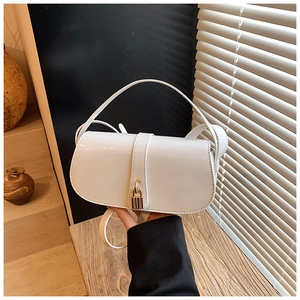 Close-up of white patent leather saddle bag with gold metal clasp and adjustable strap