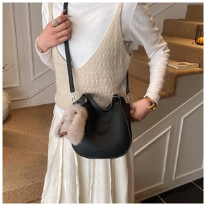 Detail of black pebbled leather bucket bag with cute plush rabbit charm on long strap