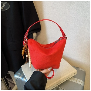Detalle de un bolso de ante rojo con colgante de cuentas de madera y cremallera plateada