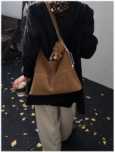 Detail of brown suede hobo bag with white contrast stitching and a plush bear charm