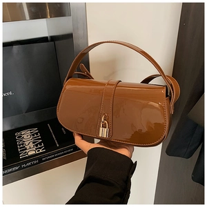 Detail of glossy brown patent leather shoulder bag with elegant golden metallic buckle