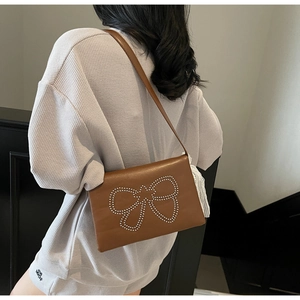 Close-up of brown leather shoulder bag featuring decorative metal rivet bow detail