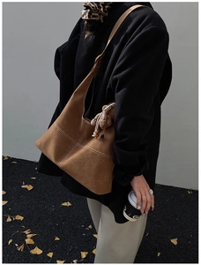 Detail of a brown suede tote bag with contrast white stitching and cute bear charm