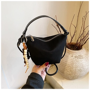 Detalle de bolso cubo negro mate con asa de cuero y colgante de cuentas de madera de colores