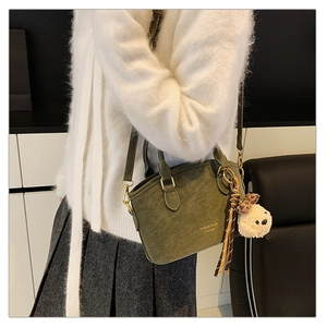 Detailed view of a dark green crossbody bag with plush dog charm and long shoulder strap