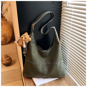 Detail of dark green matte leather shoulder bag with white contrast stitching and bear charm